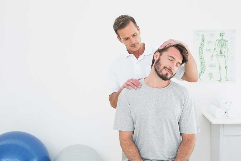 Person seated at a desk, practicing a gentle neck stretch with proper ergonomic setup visible.